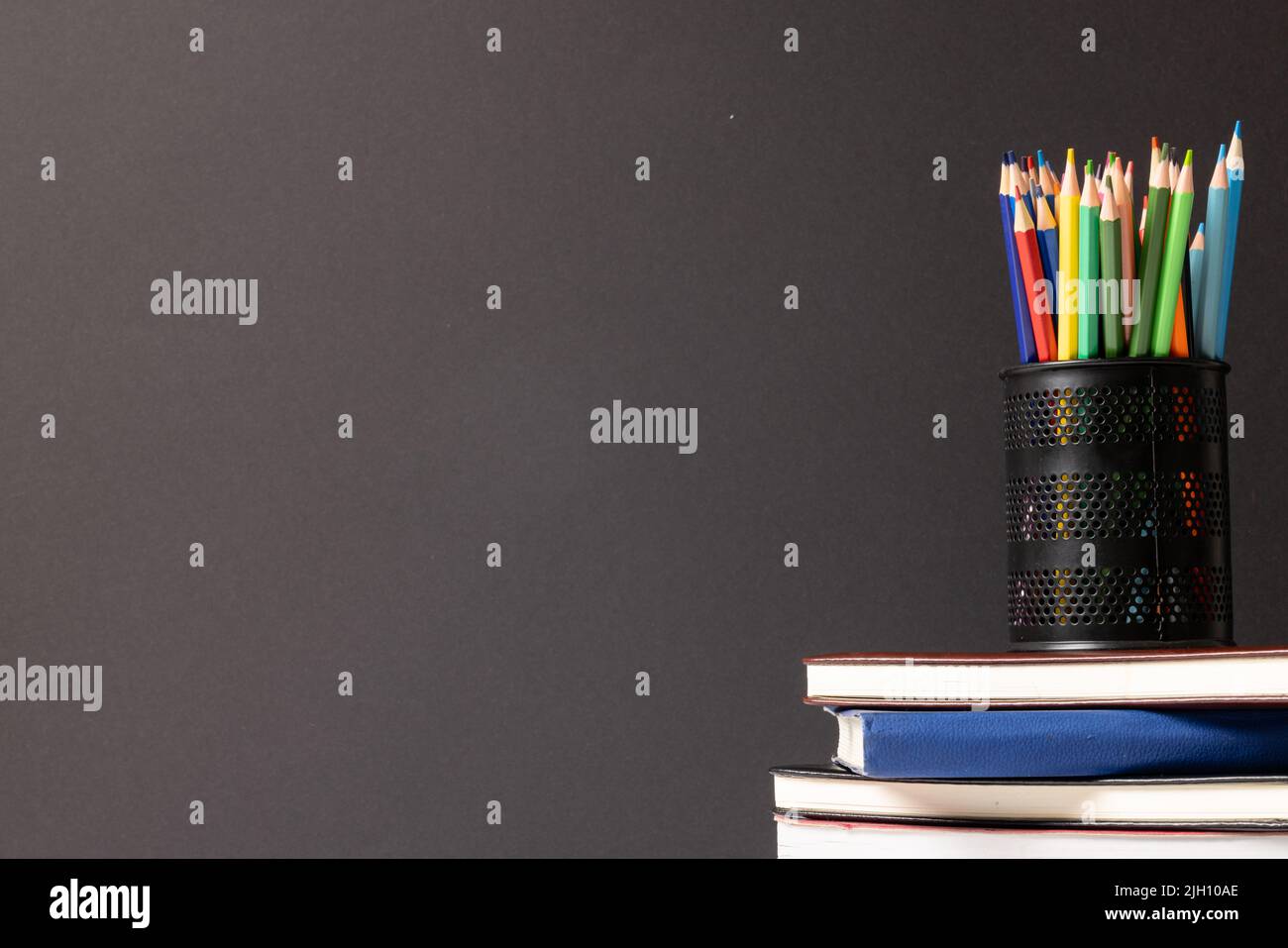 Video der Komposition der Buntstifte im Behälter auf dem Stapel der Bücher auf dem grauen Hintergrund Stockfoto