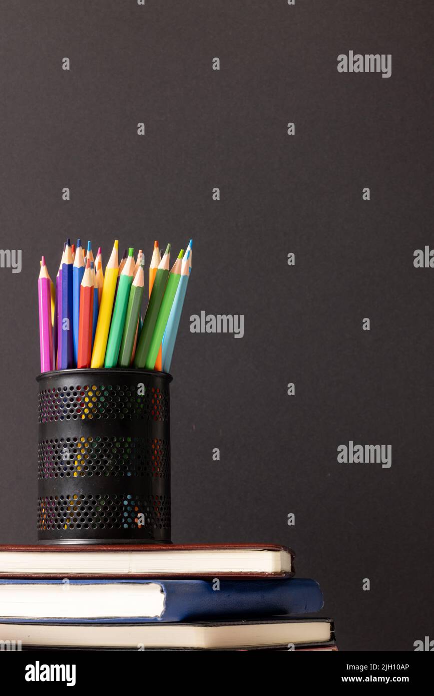 Vertikales Video der Komposition der Wachsmalstifte im Behälter auf dem Stapel der Bücher auf grauem Hintergrund Stockfoto