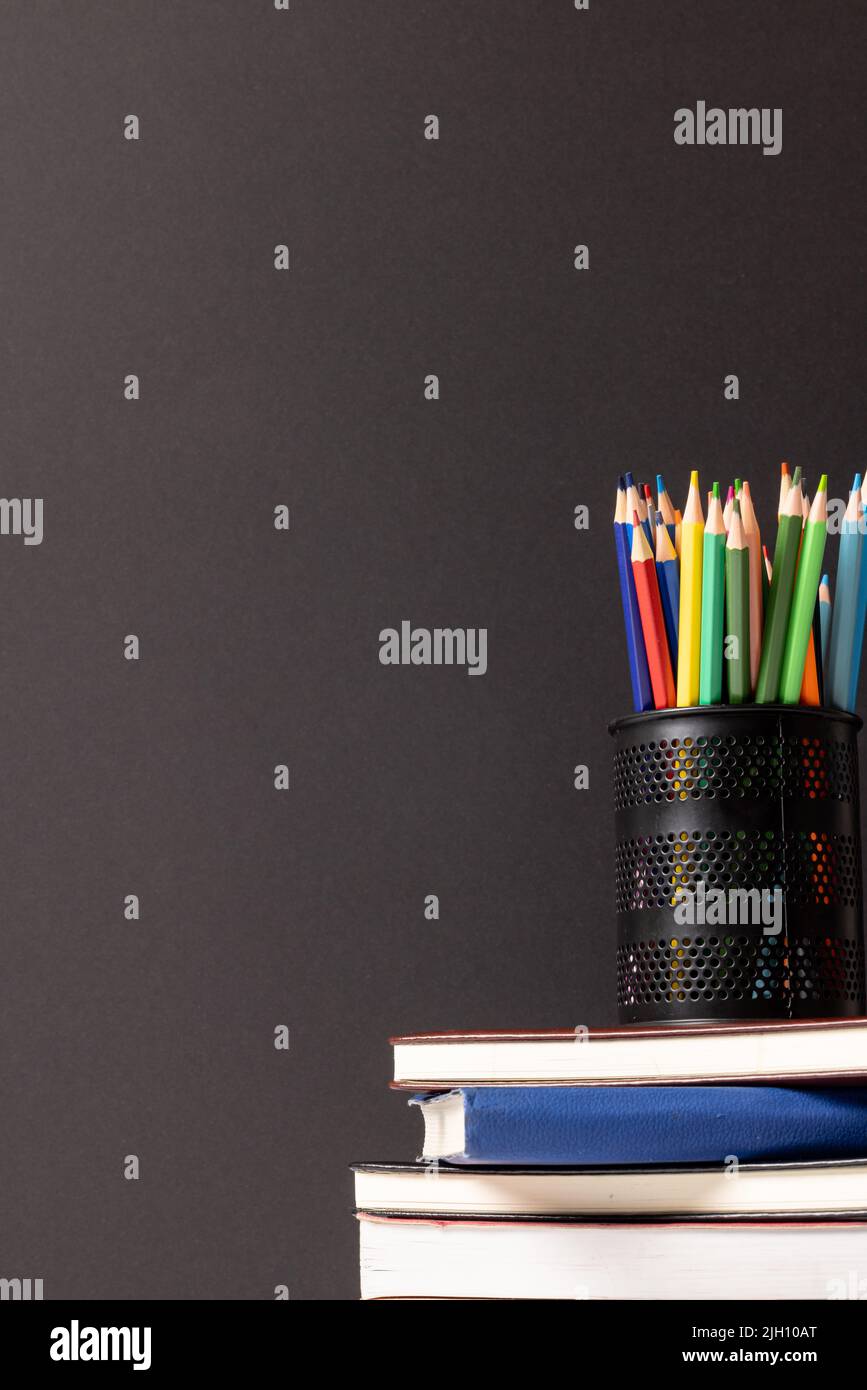 Vertikales Video der Komposition der Wachsmalstifte im Behälter auf dem Stapel der Bücher auf grauem Hintergrund Stockfoto