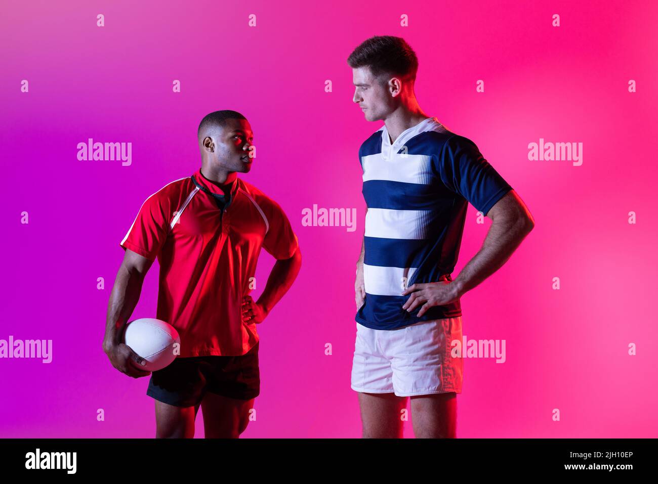Verschiedene männliche Rugby-Spieler mit Rugby-Ball über rosa Beleuchtung Stockfoto