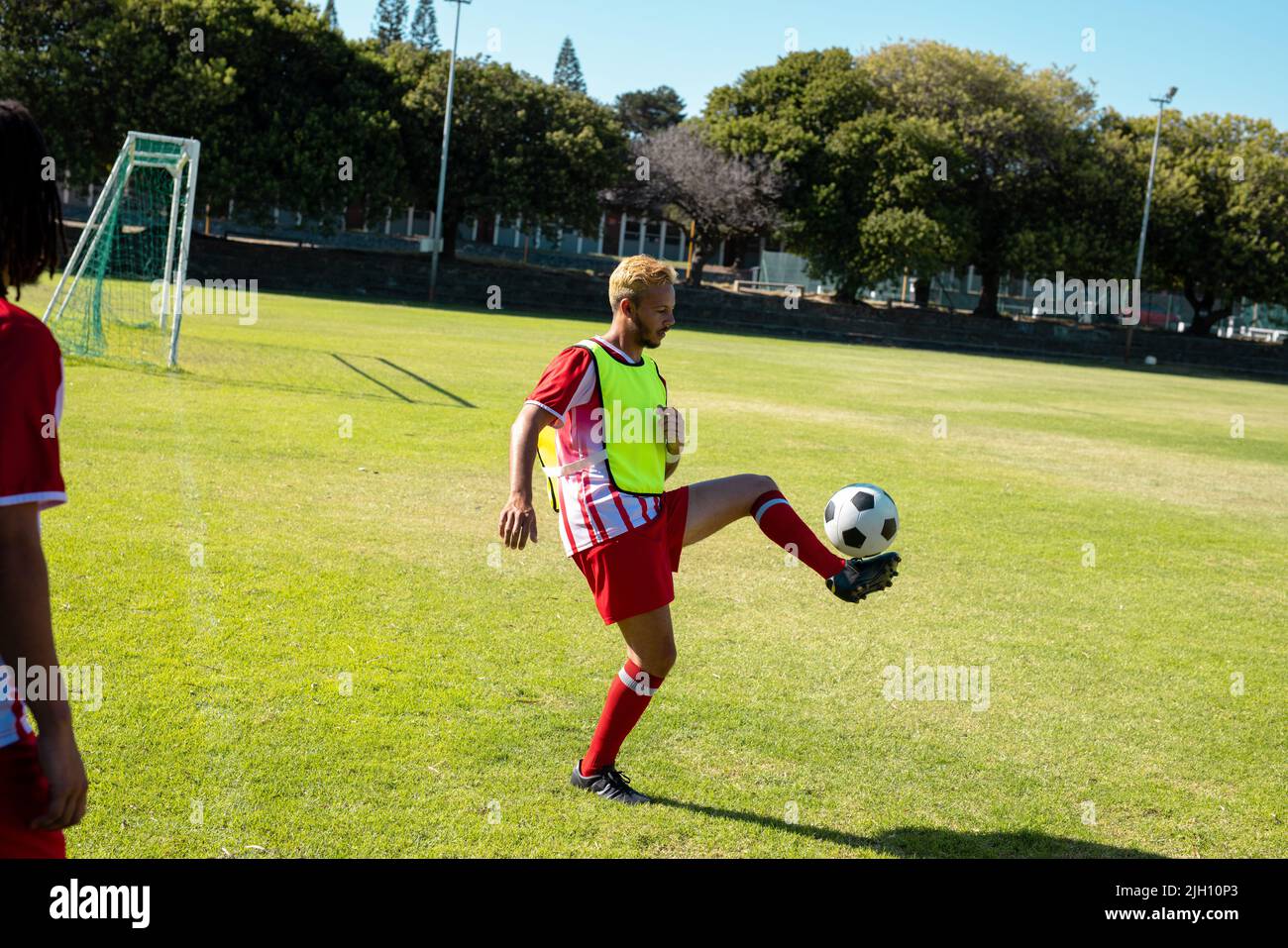 Die ganze Länge des kaukasischen jungen männlichen Spielers übt auf dem Rasen auf dem Spielplatz Freestyle-Fußball Stockfoto