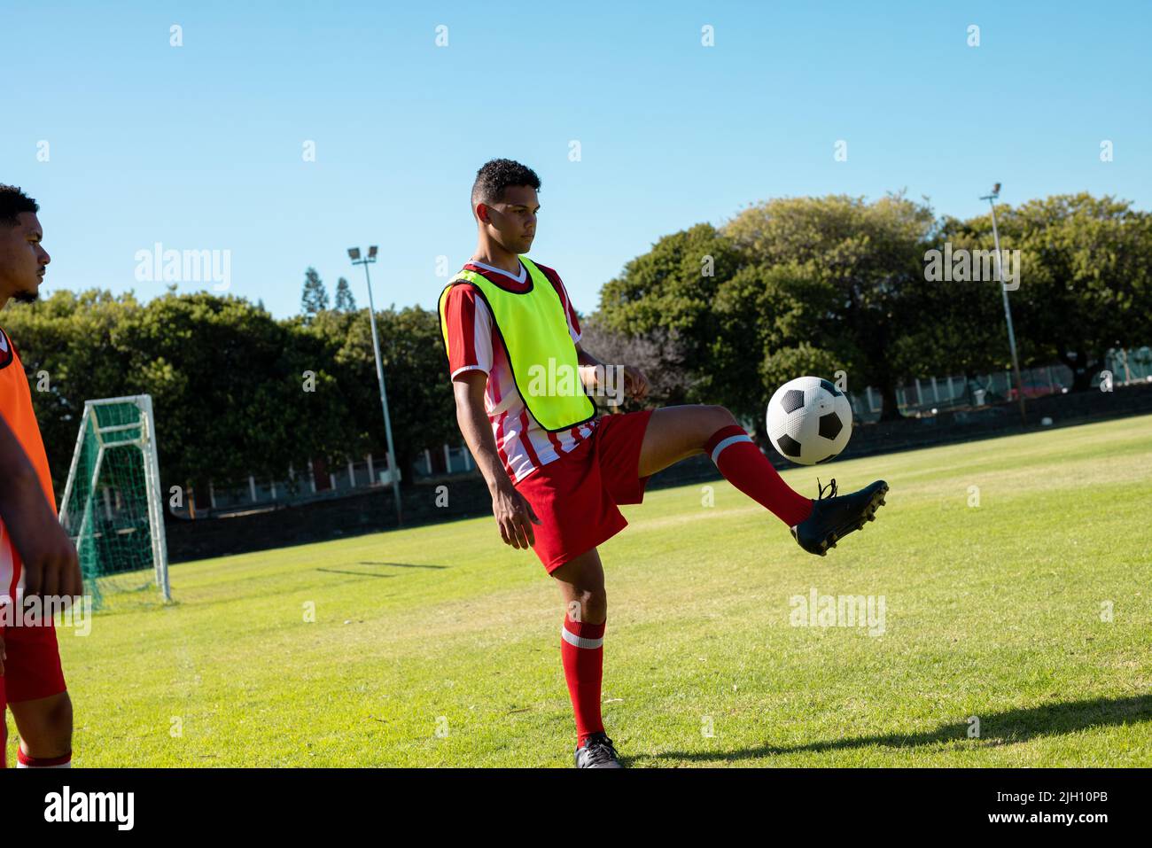 Kaukasischer Spieler, der seinen Teamkollegen beim Freestyle-Fußball auf dem Spielplatz bei klarem Himmel ansieht Stockfoto