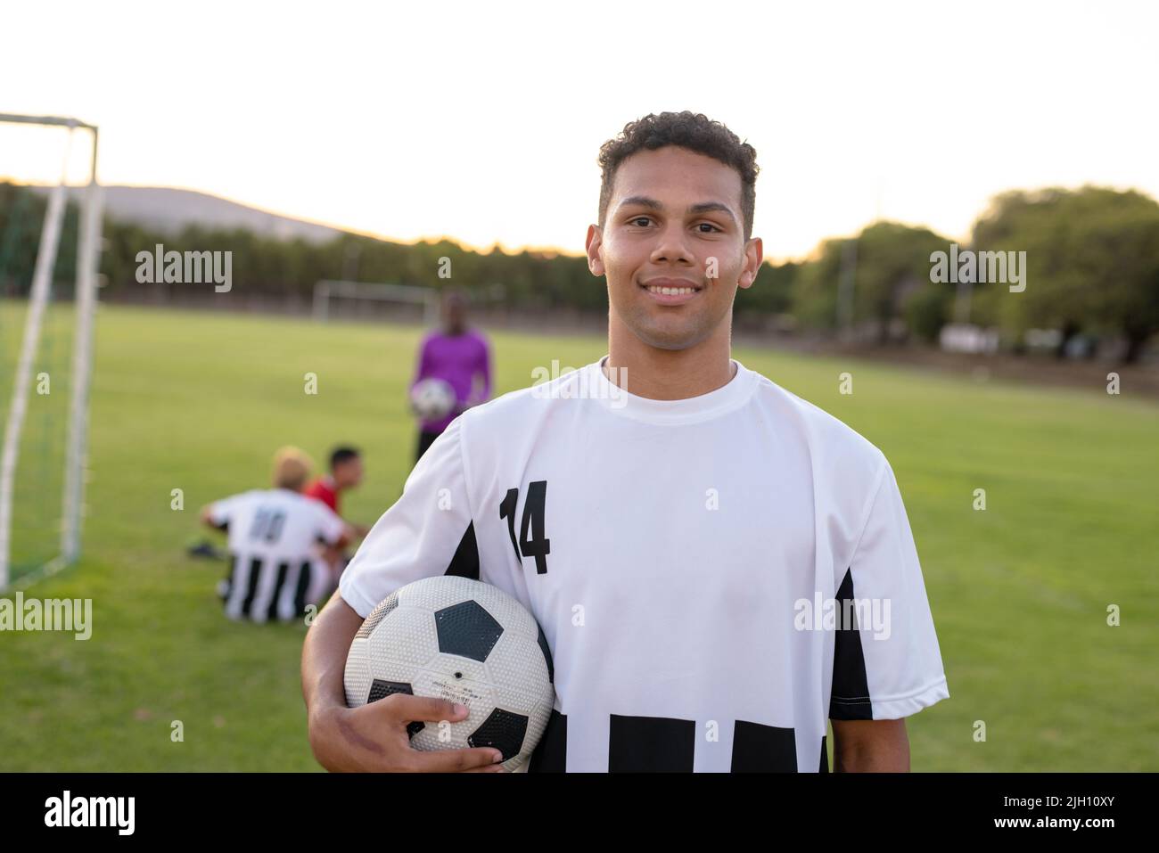 Porträt eines kaukasischen lächelnden männlichen Spielers in weißer Uniform, der den Fußball gegen den klaren Himmel hält Stockfoto