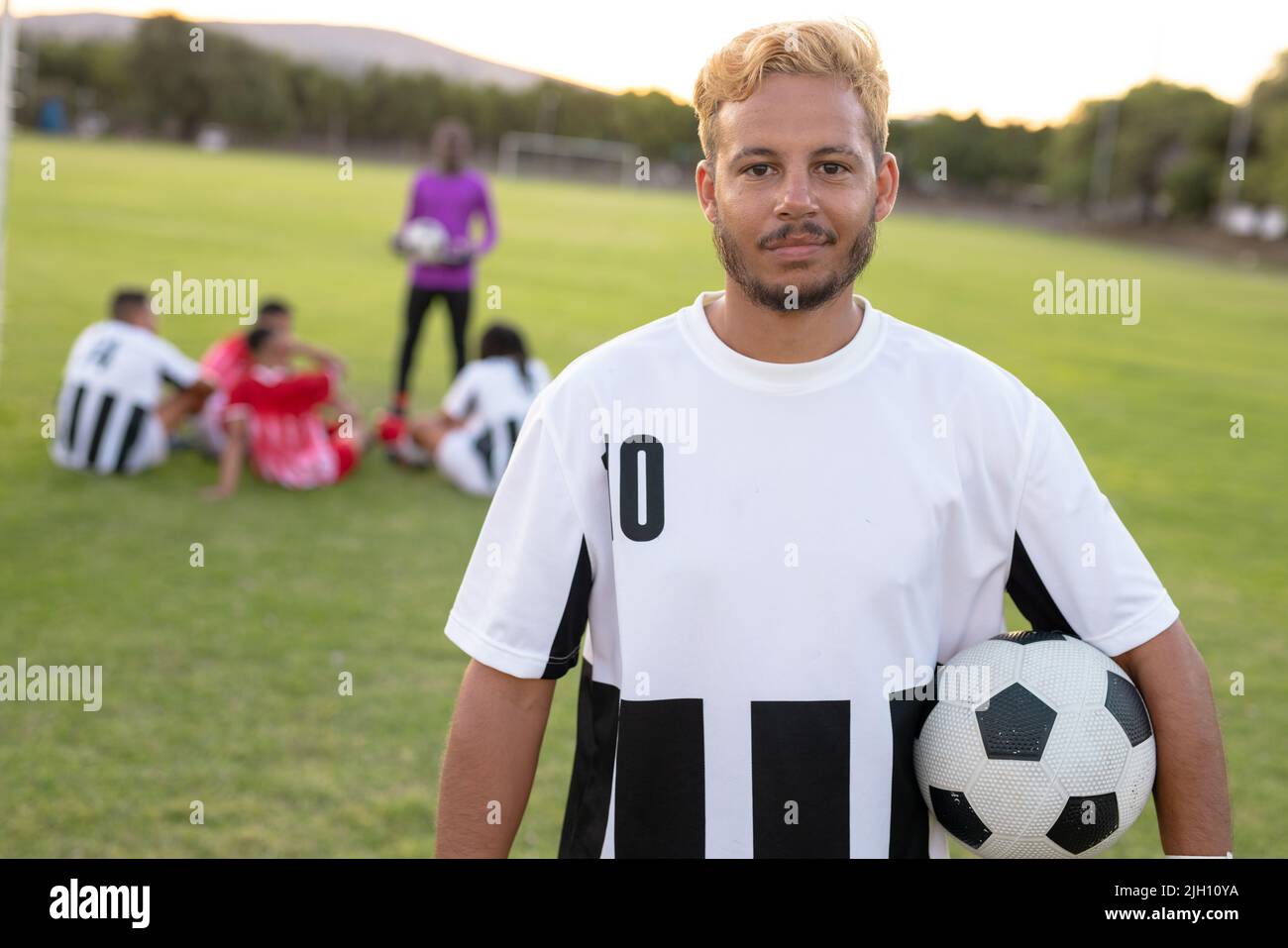 Porträt eines kaukasischen männlichen Spielers in weißer Uniform mit Fußballball, der auf dem Spielplatz steht Stockfoto