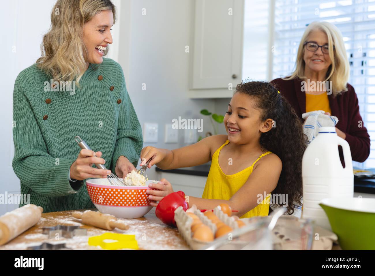 Multirassische ältere Frau, die glückliche Tochter und Enkelin beim Mischen von Essen in einer Schüssel in der Küche ansieht Stockfoto