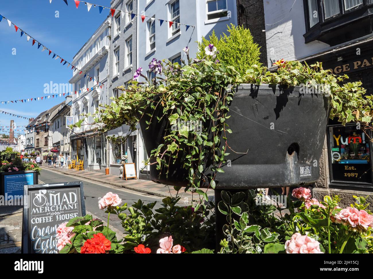 Blumentübel und Verblumungen bringen ein festliches Feeling in die Southside Street auf Plymouth historischem Barbican. Eine schrullige Mischung aus kleinen Geschäften, öffentlichen Häusern und r Stockfoto