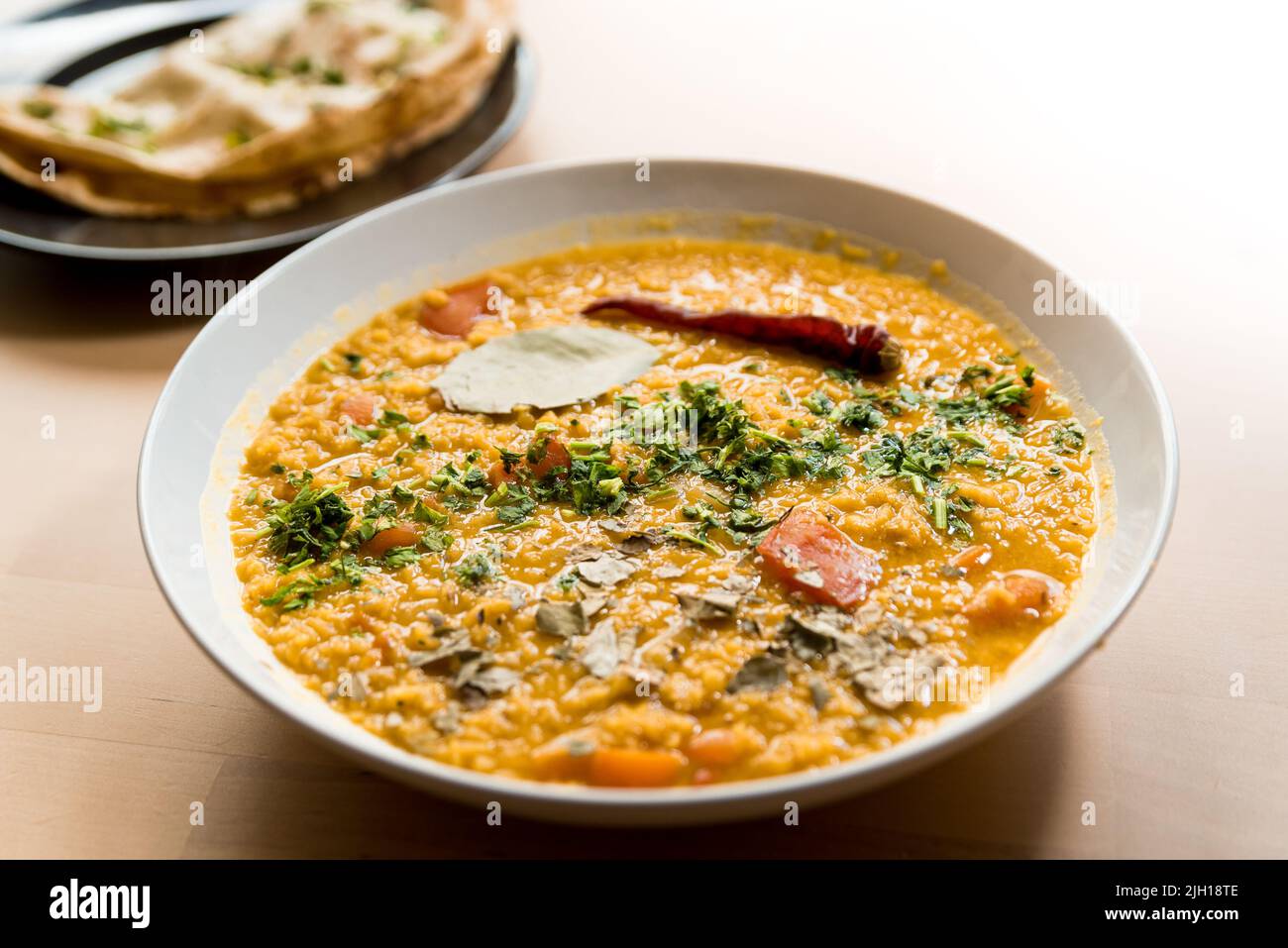 Traditionelles indisches dal hausgemacht. Traditionelle indische Suppenlinsenschalen. Indisches Dhal würziges, in einer Schüssel mit Koriander und Gewürzen auf einem Holztisch mit Roti. Stockfoto