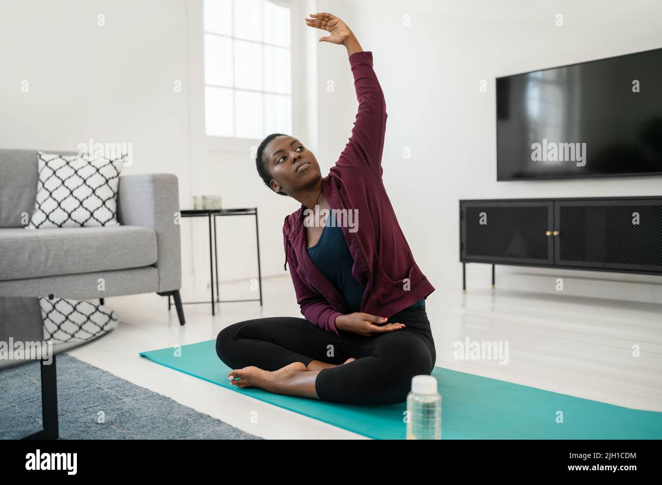 Nahaufnahme einer schwarzen afrikanischen Frau, die in einer dehnenden Yoga-Pose auf einer Matte im Wohnzimmer sitzt, Stretching und Meditation zu Hause beim Workout Stockfoto