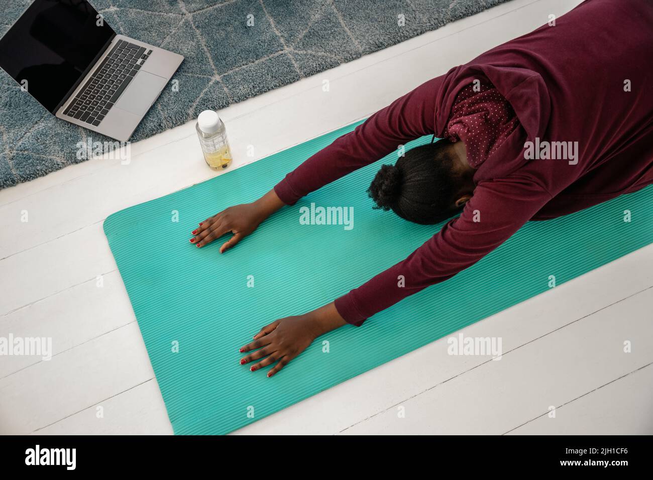 Junge schwarze afrikanische Frau macht Yoga-Übungen online. Stretching zu Hause auf der Matte vor dem Laptop-Computer, direkt von oben aufgenommen. Stockfoto