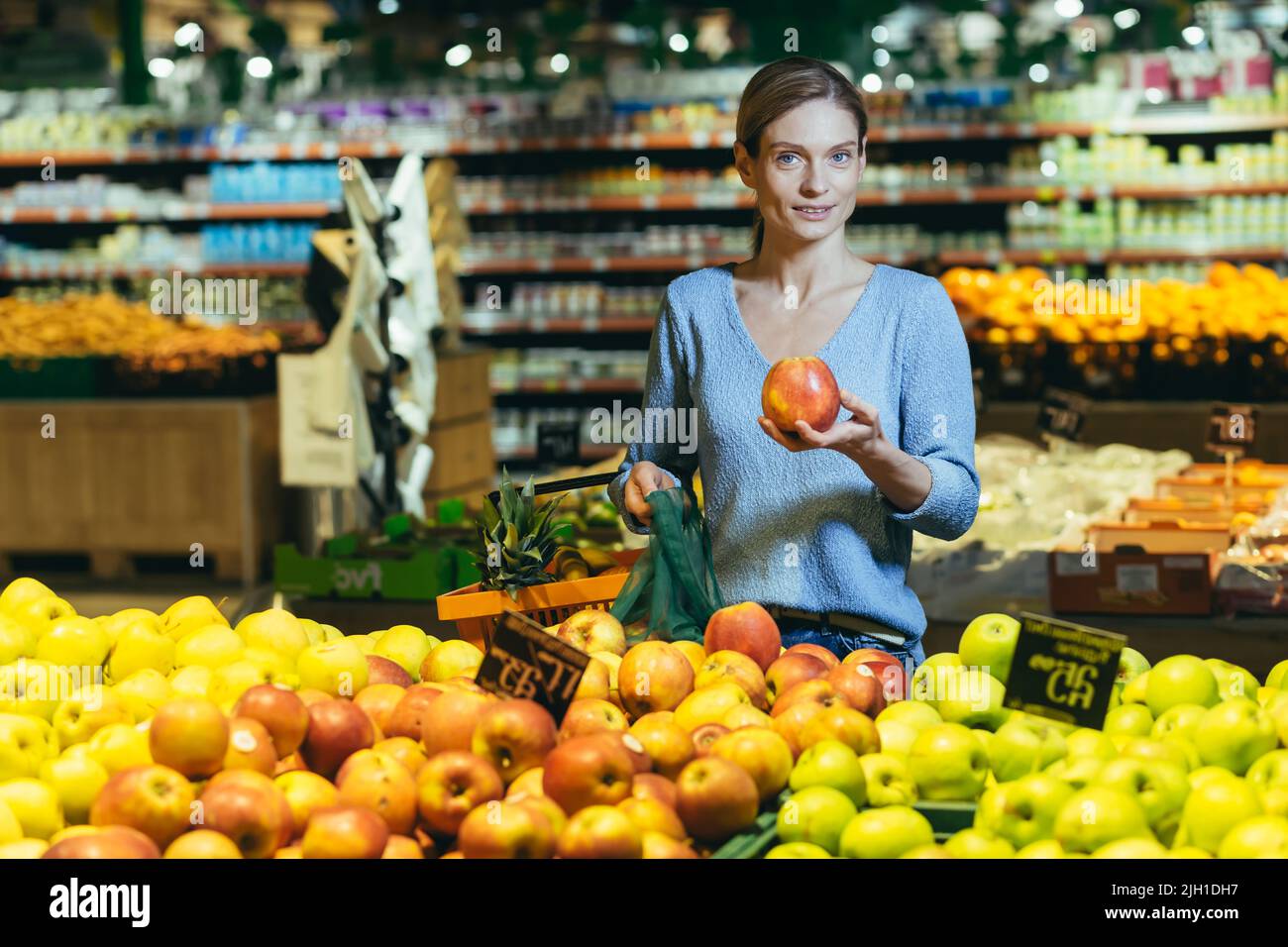 Frau wählt Obst Gemüse auf der Theke im Supermarkt. Weibliche Hausfrau einkaufen auf dem Markt in der Nähe von Gemüse Kaufhaus mit einem Korb in den Händen. Untersucht Apfel Stockfoto
