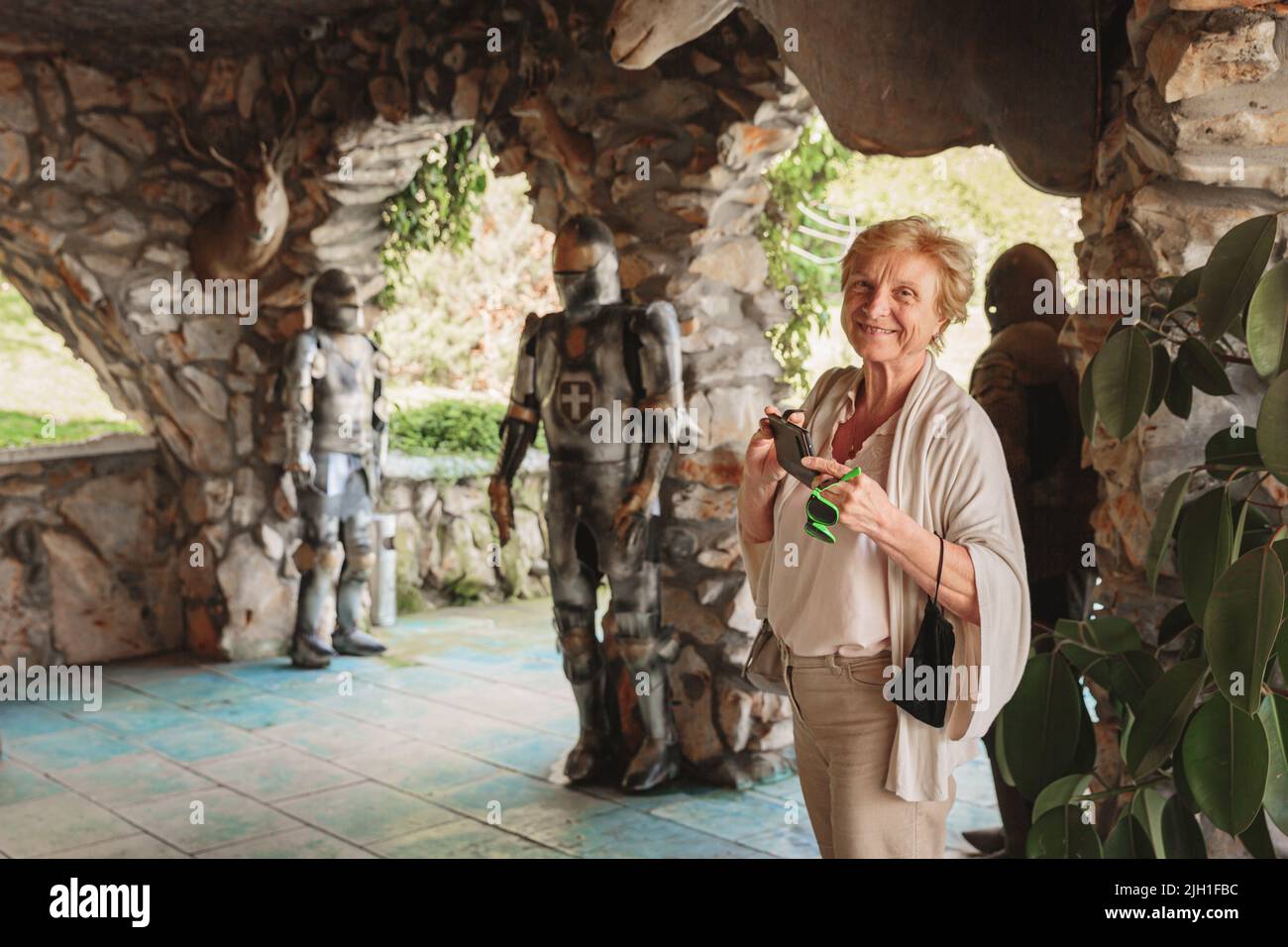 Ältere Touristenfrau, die in einem alten Schloss Fotos auf ihrem Telefon machte Stockfoto