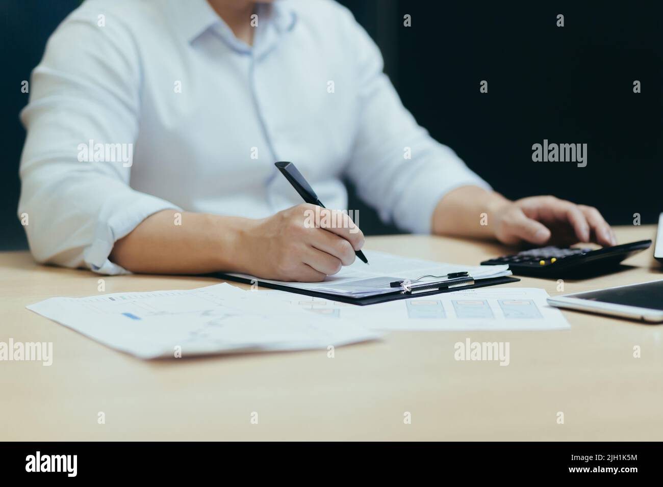 Nahaufnahme. Die Hände eines jungen Mannes ein Buchhalter in einem weißen Hemd, der an einem Schreibtisch mit Dokumenten, einem Taschenrechner, arbeitet, schreibt. Sitzen in einem modernen Büro Stockfoto