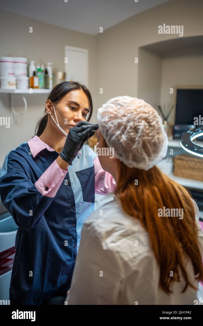 Der Meister des Permanent Make-up-Kosmetologen nimmt Messungen für die neue Form der Augenbrauen des Modells vor. Vorbereitung der Mikrobladenbehandlung Stockfoto