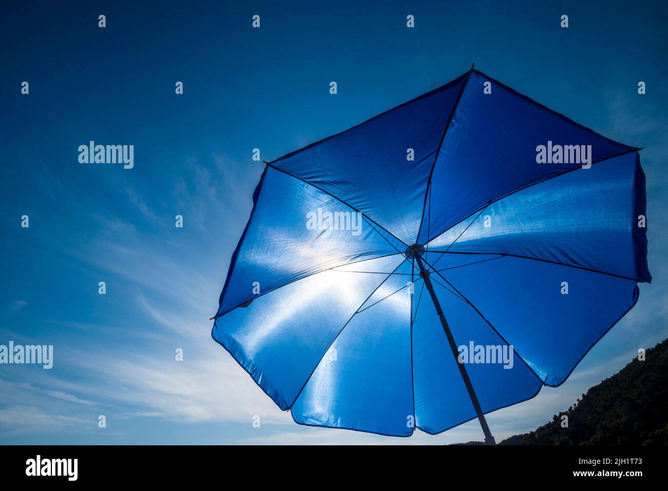 Leuchtender blauer Sonnenschirm gegen die Sonne Stockfoto