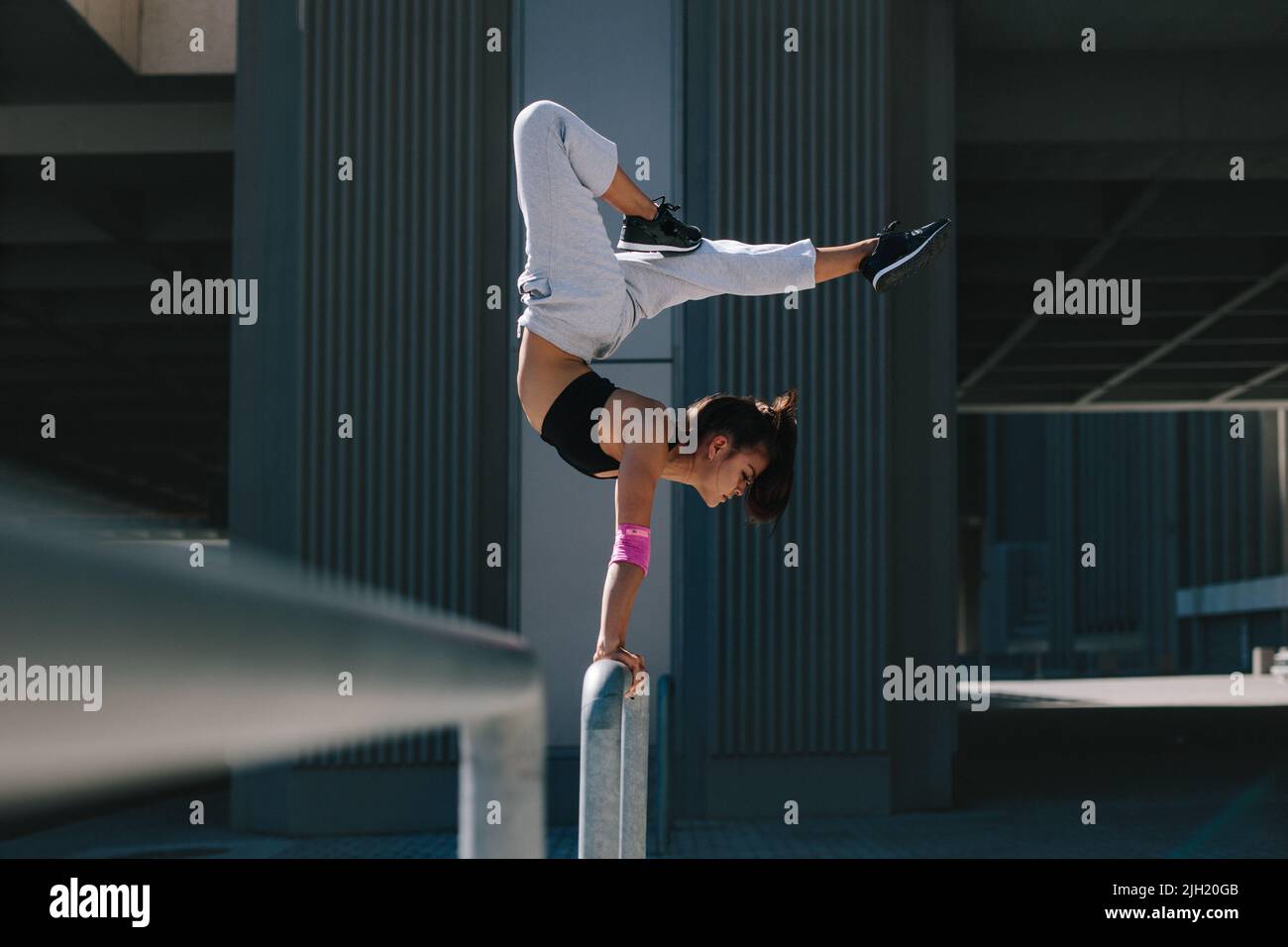 Sportlerin, die einen Handstand auf Geländer im Freien macht. Flexible weibliche Athletin, die Extremsport in einem städtischen Raum ausführt. Stockfoto
