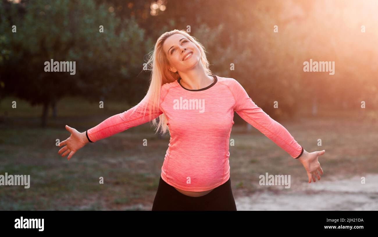 Glückliche, schwanger Frau, die den Moment, den Sonnenuntergang genießt Stockfoto