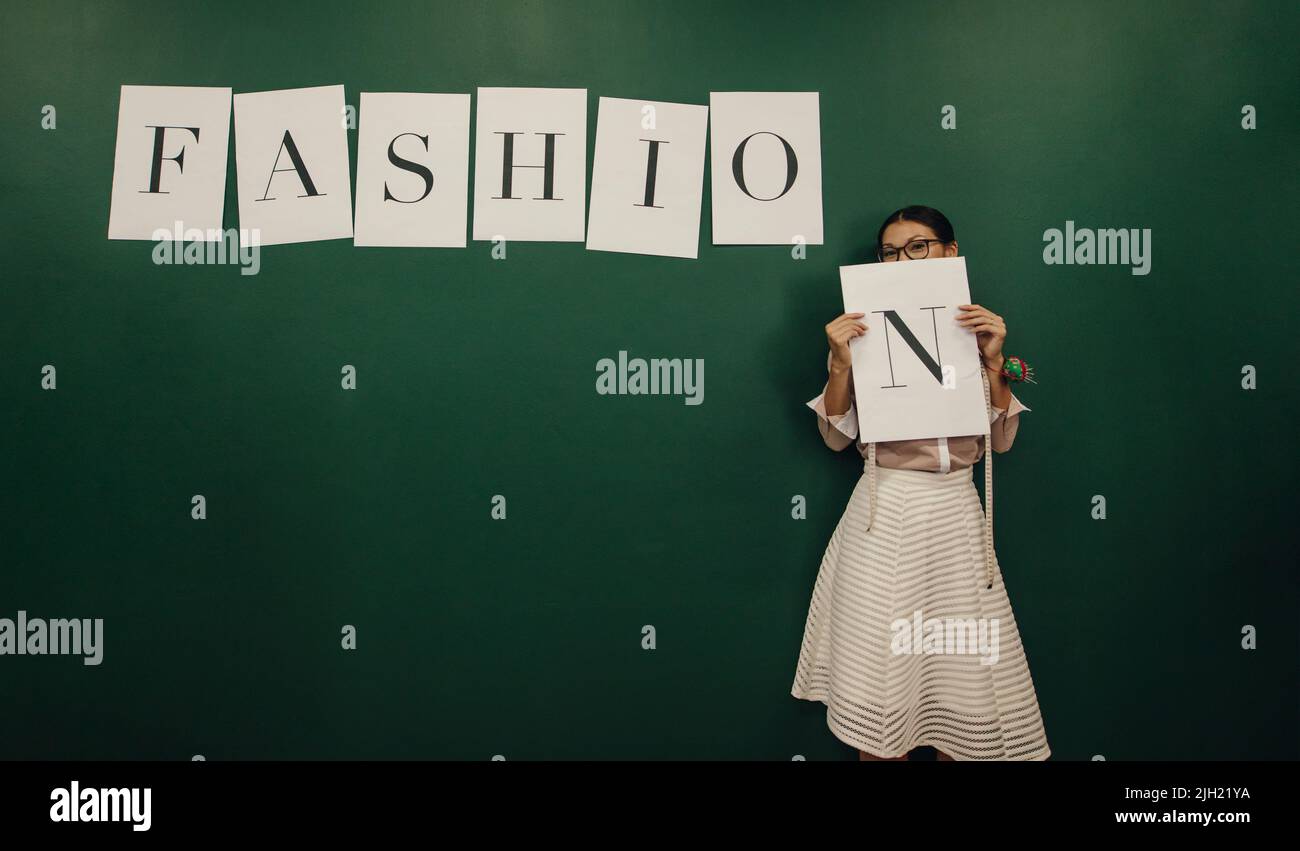 Eine Modedesignerin, die ein Plakat mit dem Buchstaben „N“ hält, während sie in einem Studio steht. Kreative weibliche Designerin kleben Alphabet Aufkleber auf die w Stockfoto