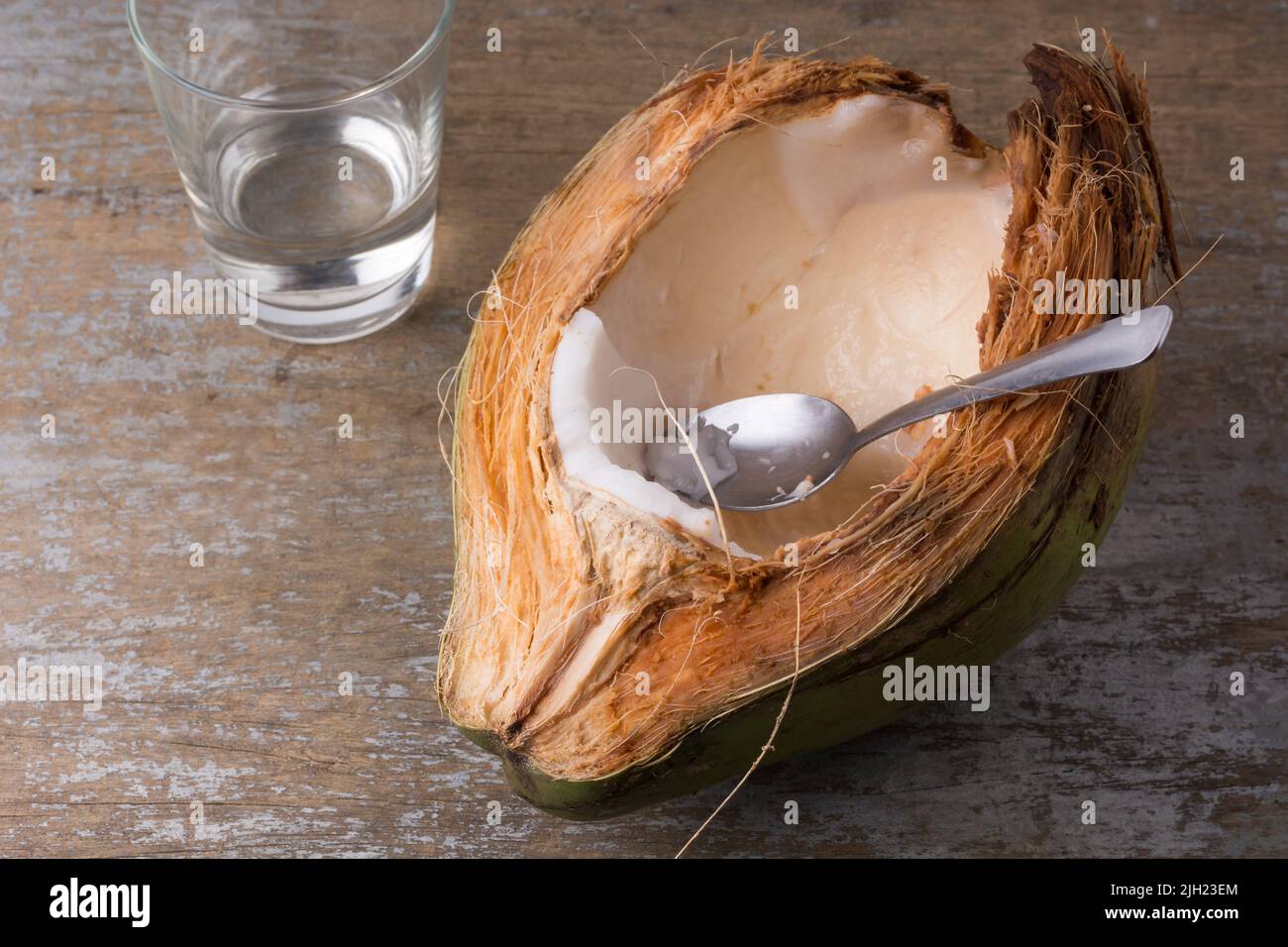 Essen von jungem Kokosfleisch direkt aus der Schale mit einem Löffel, weißes Fleisch von gesunden tropischen Früchten auf einer Holztischplatte, Platz für Text Stockfoto