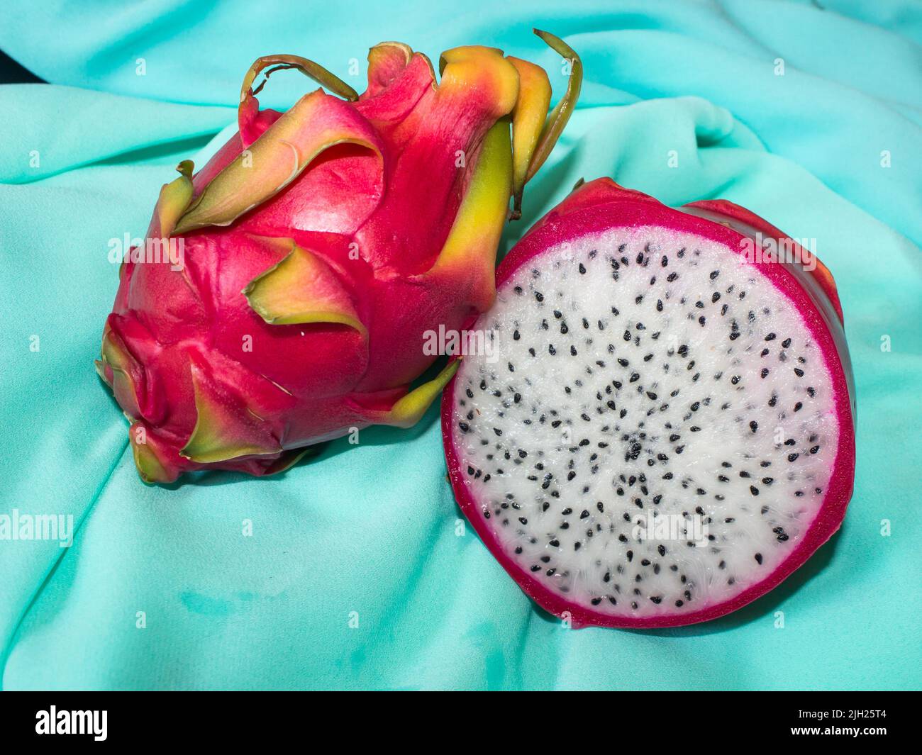 Ein Ganzes und eine geschnittene Drachenfrucht auf einem türkisfarbenen Stück Stoff Stockfoto