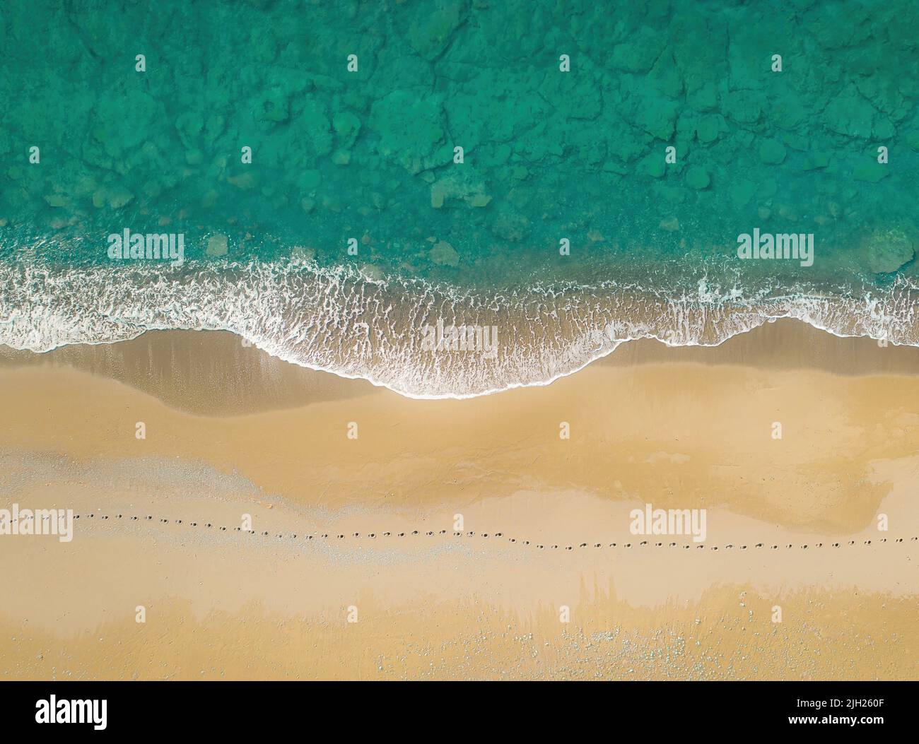 Menschliche Fußabdrücke an einem sandigen Ufer entlang des Meeres mit brechenden Wellen. Luftaufnahme direkt darüber Stockfoto