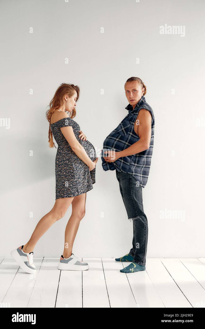 Eine Schwangeren und ihr Mann machen lustige Schwangerschaftsfotos. Der Mann zeigt seinen Bauch vor der Schwangeren Stockfoto