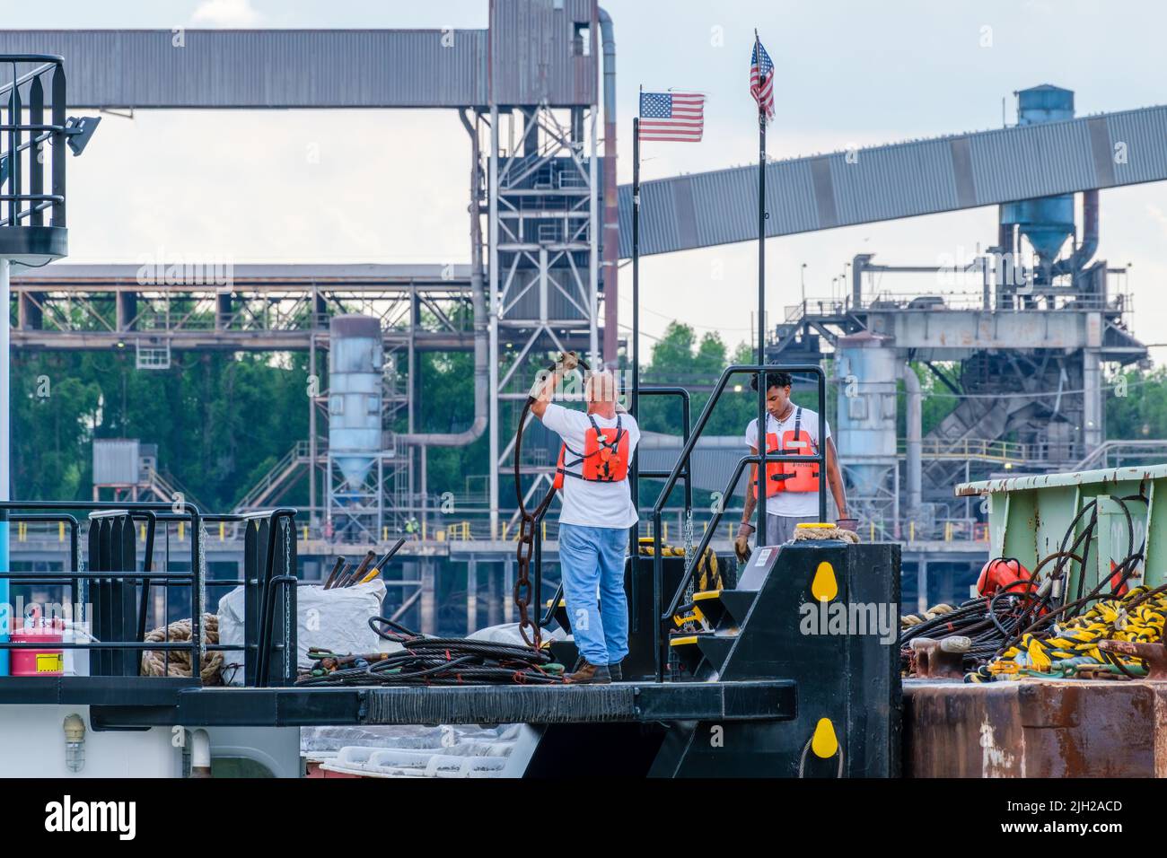 NEW ORLEANS, LA, USA - 11. JULI 2022: Schlepper-Deck-Crew bei der Arbeit neben einem Lastkahn auf dem Mississippi River mit einem Getreideaufzug im Hintergrund Stockfoto