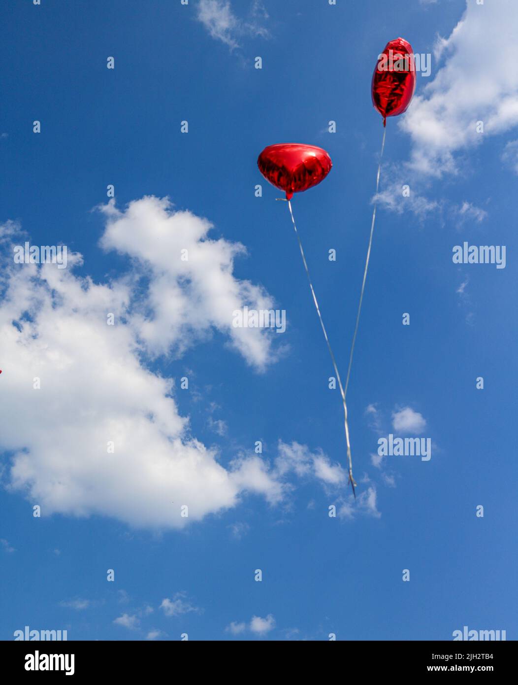 Zwei rote Luftballons in Herzform vor einem blauen Sommerhimmel mit weißen Schönwetterwolken Stockfoto