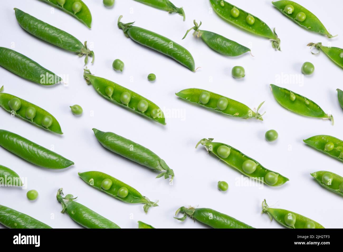 Rotierende junge grüne Erbsen auf weißem Hintergrund, gesundes Lebensmittelkonzept, trendiger Gemüsehintergrund. Stockfoto