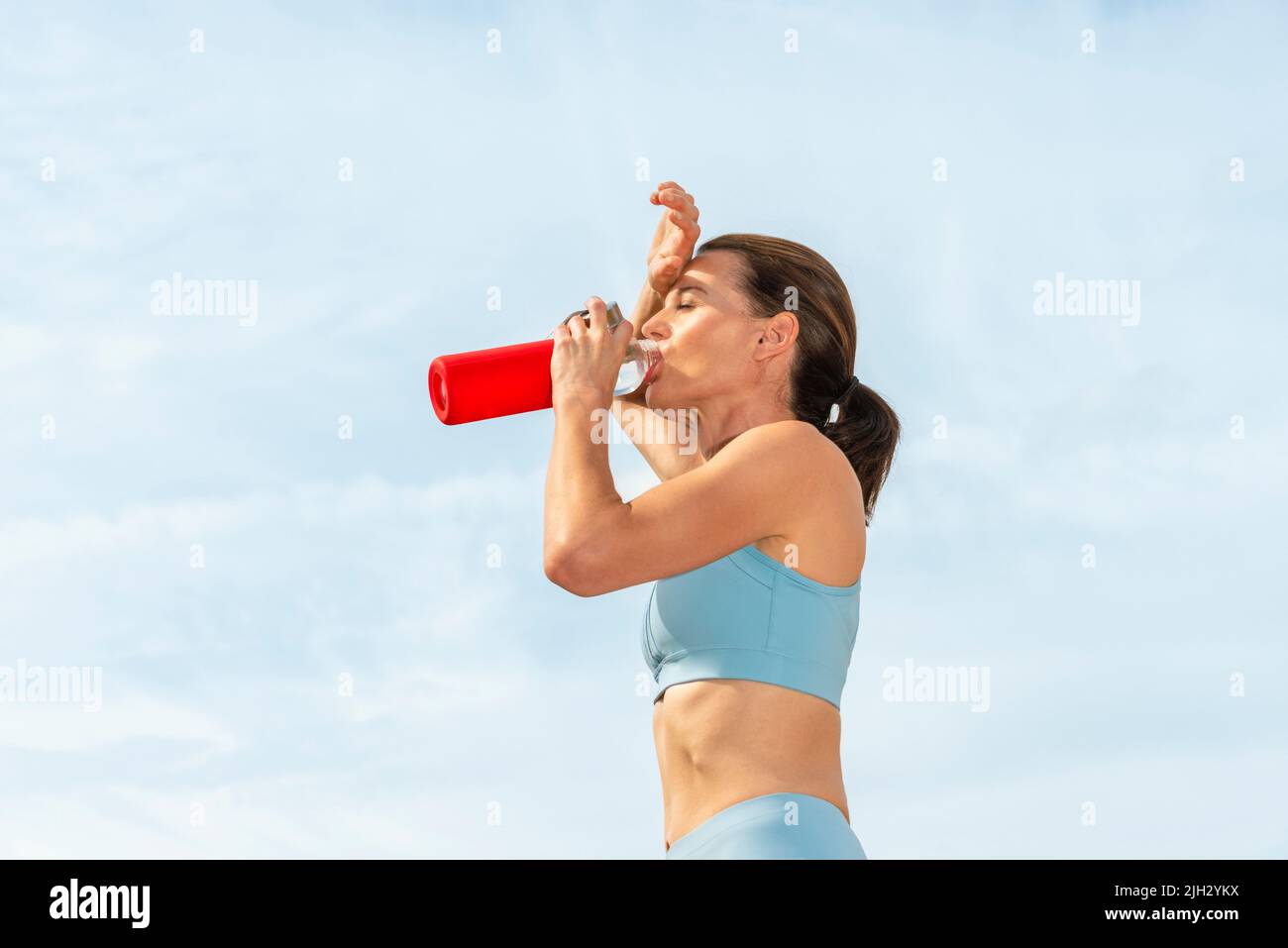 Sportliche Frau, die die Auswirkungen der Sonne spürt und ein Getränk mit Wasser nimmt. Stockfoto