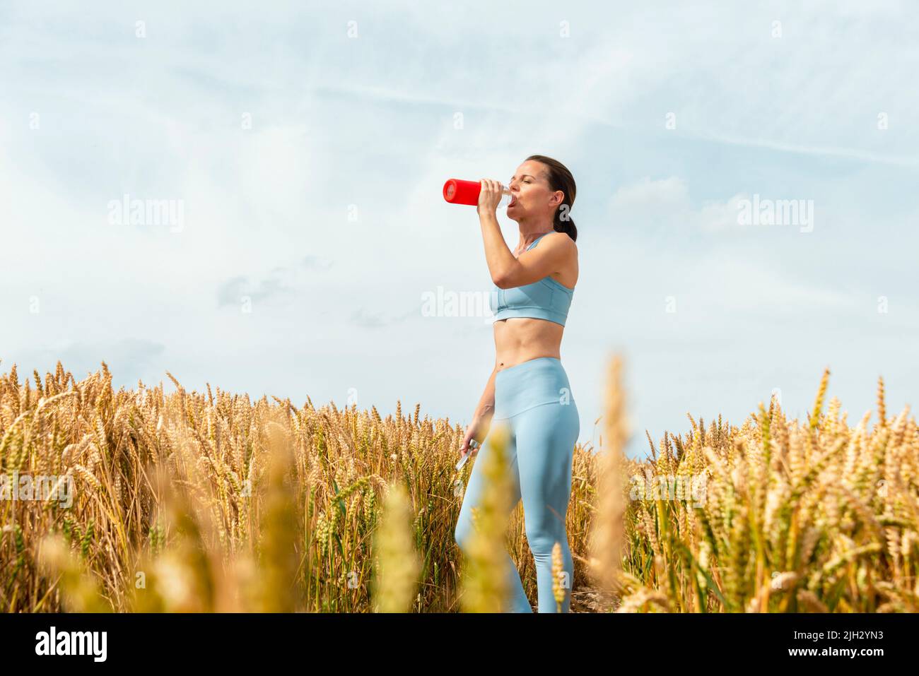 Sportliche Frau auf dem Land trinkt Wasser aus einer Glasflasche. Stockfoto