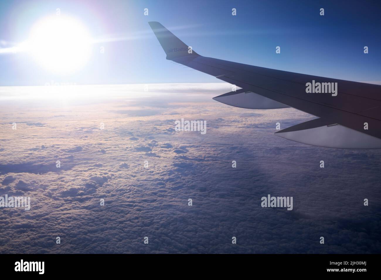 Airbus A220-300 Flügel in Sonnenuntergangslichtern fliegen über Wolken irgendwo über der Ostseeregion in Europa Stockfoto