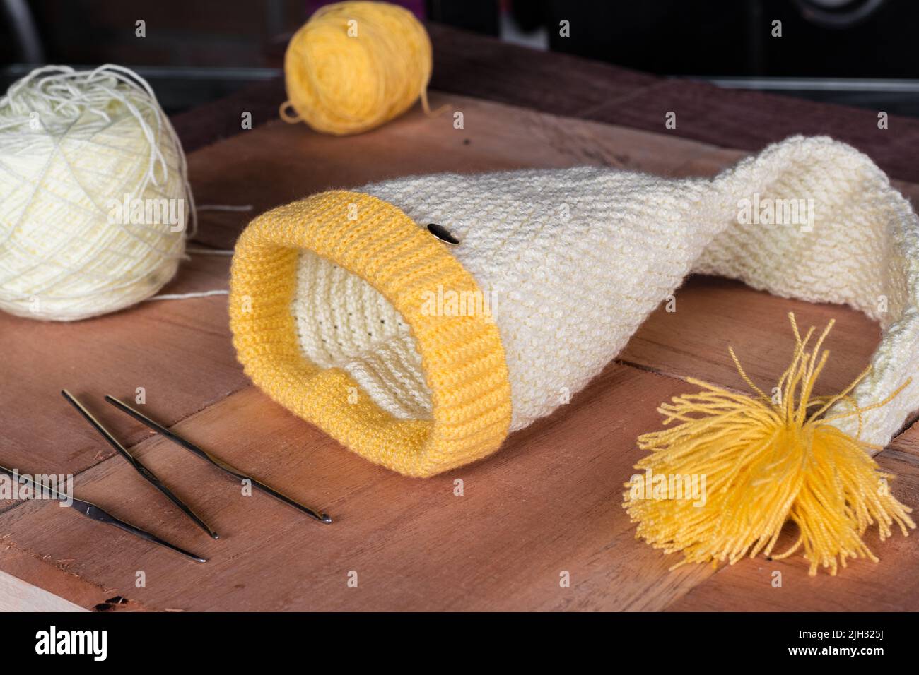 Weiß und gelb gehäkelt gestrickt Winterhut, zusammen mit Materialien zu entwerfen und zu Hause stricken. Wollhut in einer länglichen Form entworfen. Home Based e Stockfoto