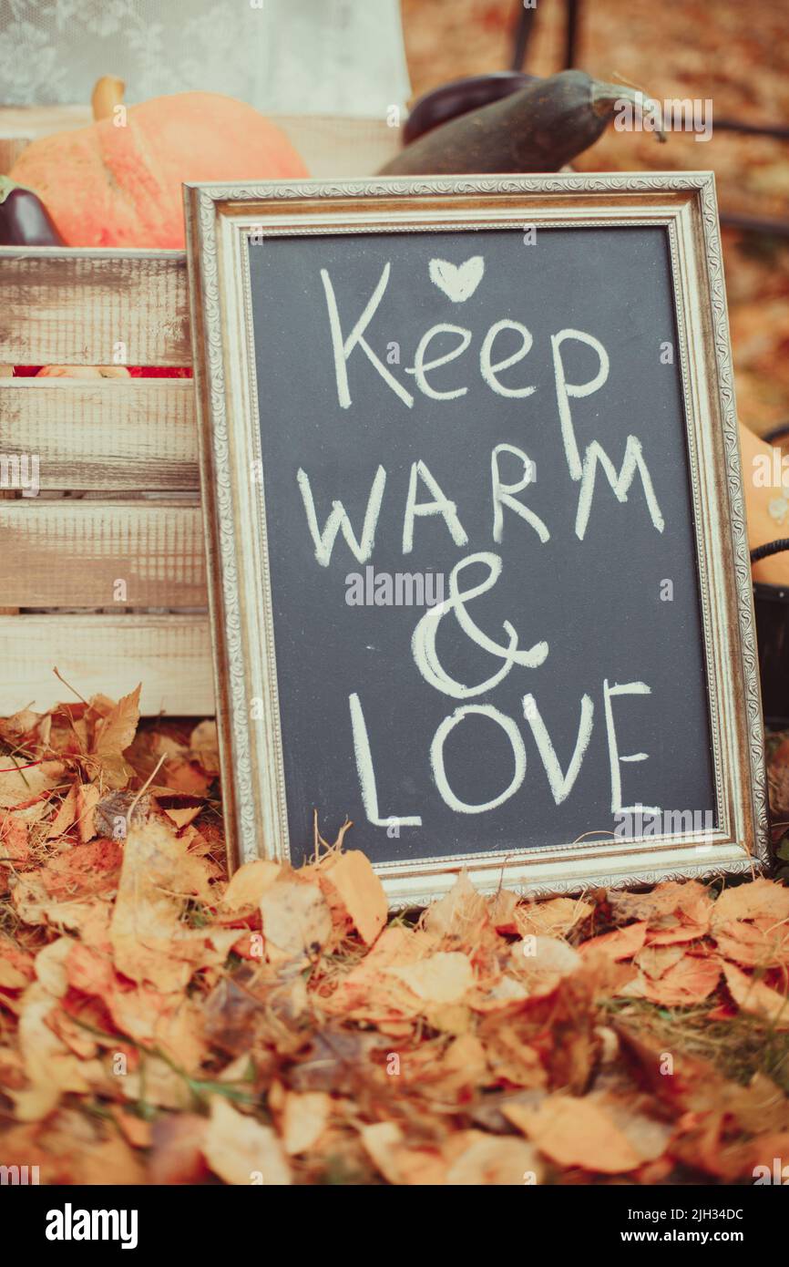 Das Brett hält sich warm und die Liebe steht in der Nähe eines Holzhauses in gelbem Laub. Poster im skandinavischen oder amerikanischen Stil mit Holzrahmen. Rustikales Vintage Stockfoto