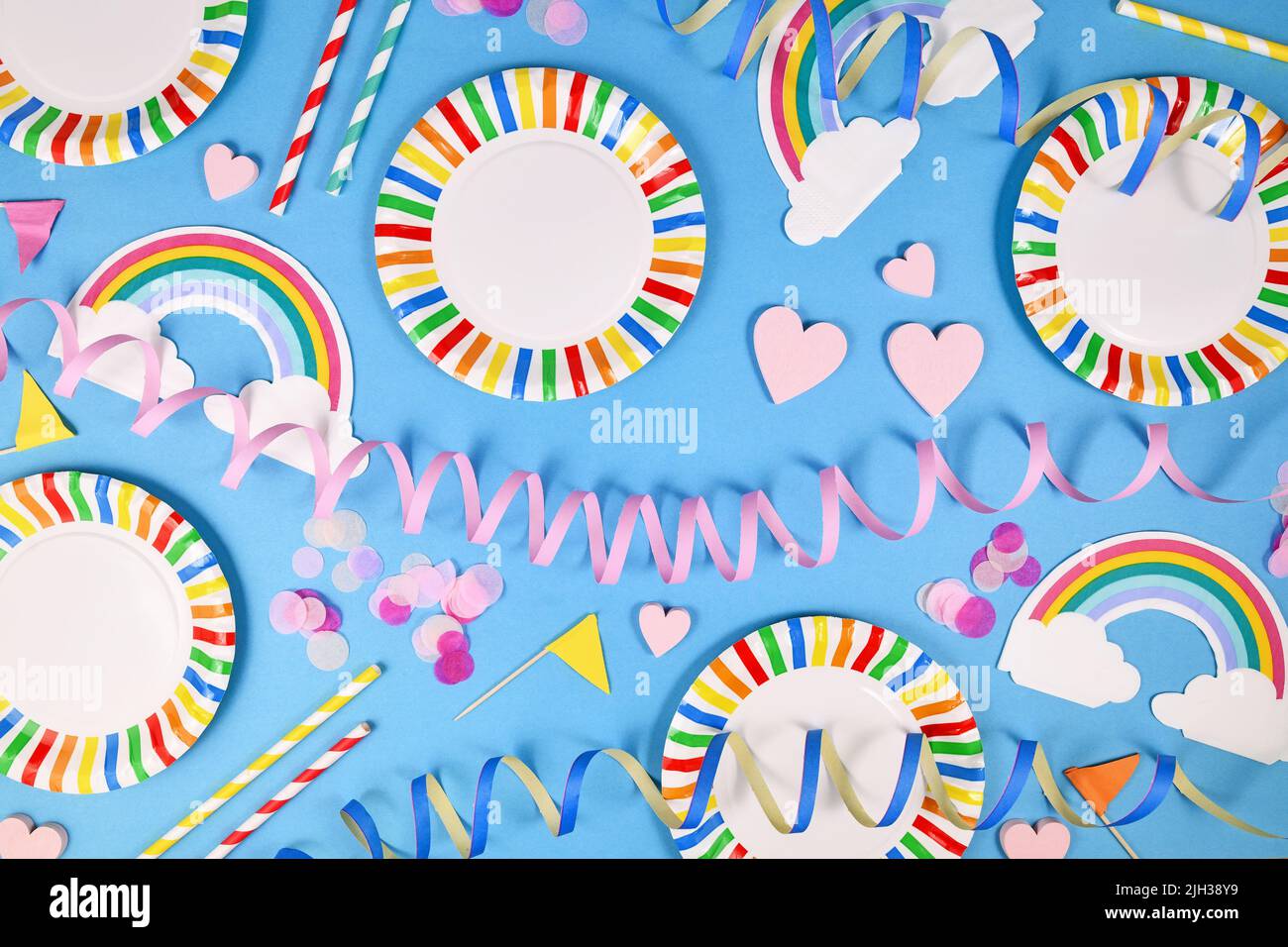Party Flat Lay mit bunten Tellern, Regenbogenservietten und Trinkhalmen auf blauem Hintergrund Stockfoto