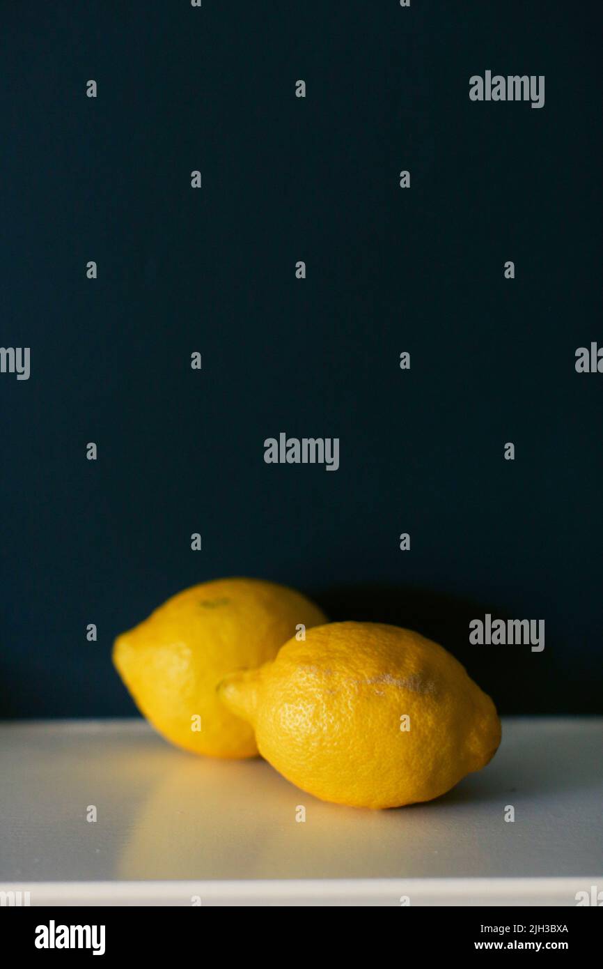 Stillleben von zwei leuchtend gelben Zitronen auf einem weißen Regal vor einem dunkelblauen Hintergrund Stockfoto