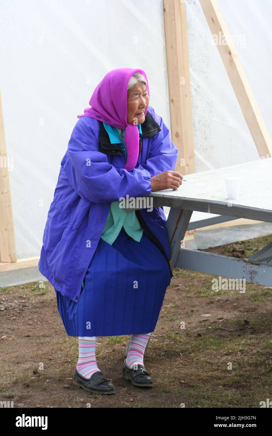 Ältere Dene-Frau aus Whati sitzt am Picknicktisch und raucht, in der nördlichen indigenen Gemeinschaft von Deline, Northwest Territories, Kanada. Stockfoto