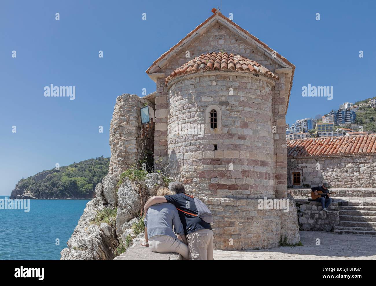 Altes, gebogenes Kirchengebäude in der Stadt Kotor mit zwei Menschen, die auf das Meer blicken Stockfoto