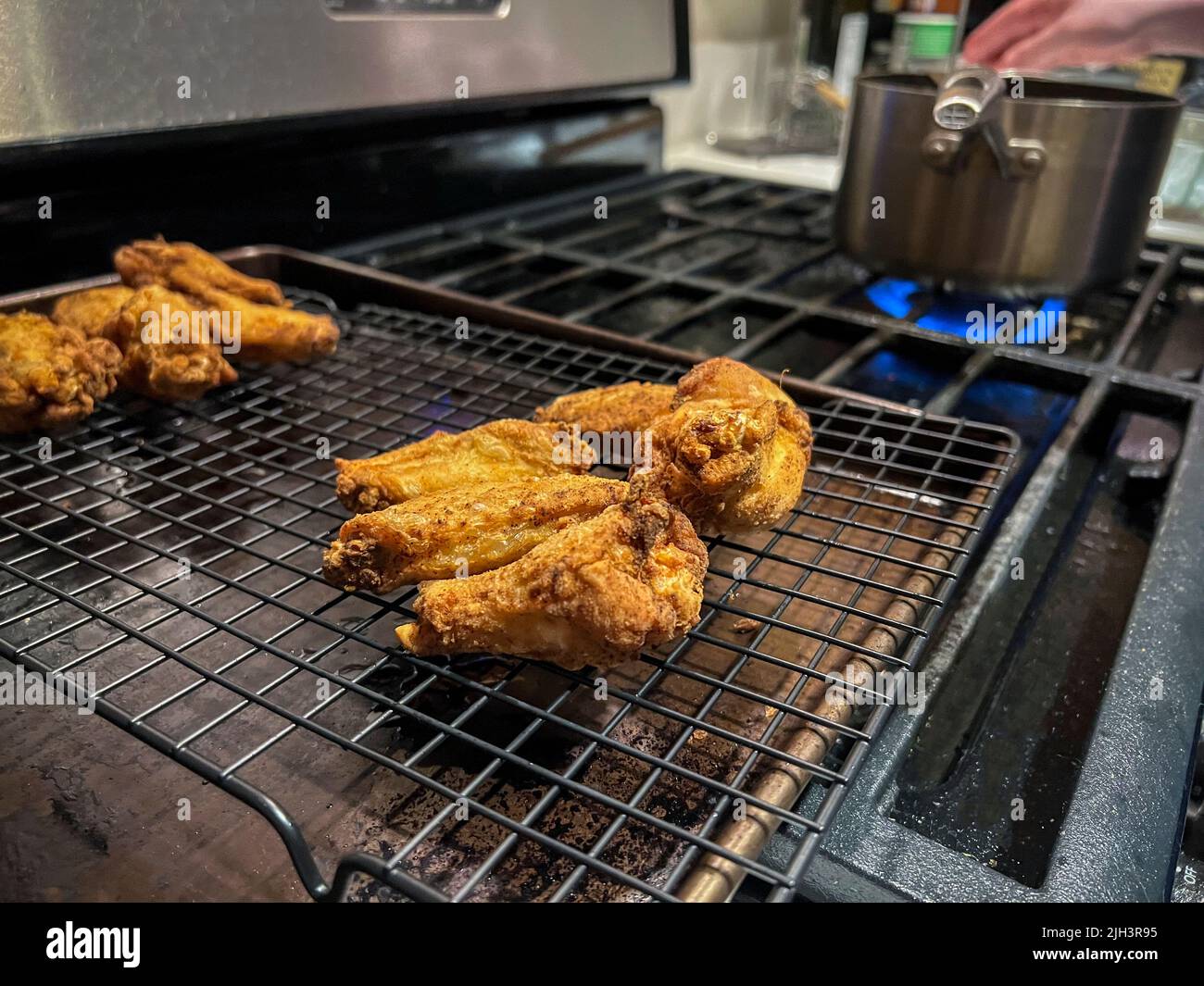Nahaufnahme, selektiver Fokus auf hausgemachte gebratene Hähnchenflügel auf einem Trockengestell in einer heimischen Küche Stockfoto