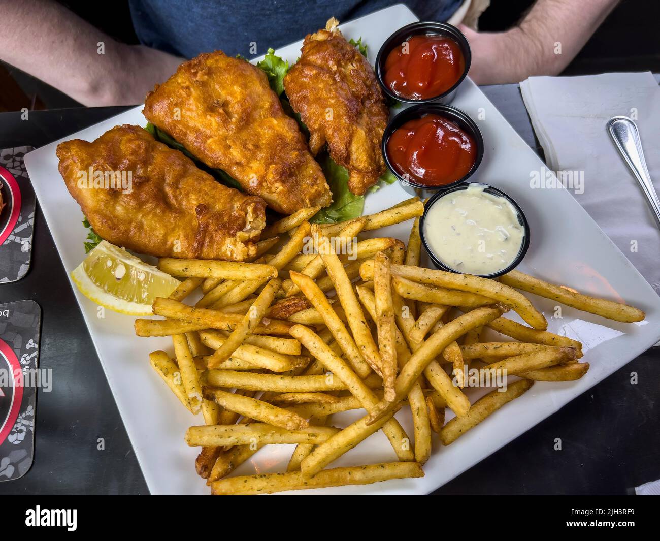 Nahaufnahme von knusprigen Fischen und Chips auf einem Tisch in einem Restaurant vor einem kaukasischen Mann Stockfoto