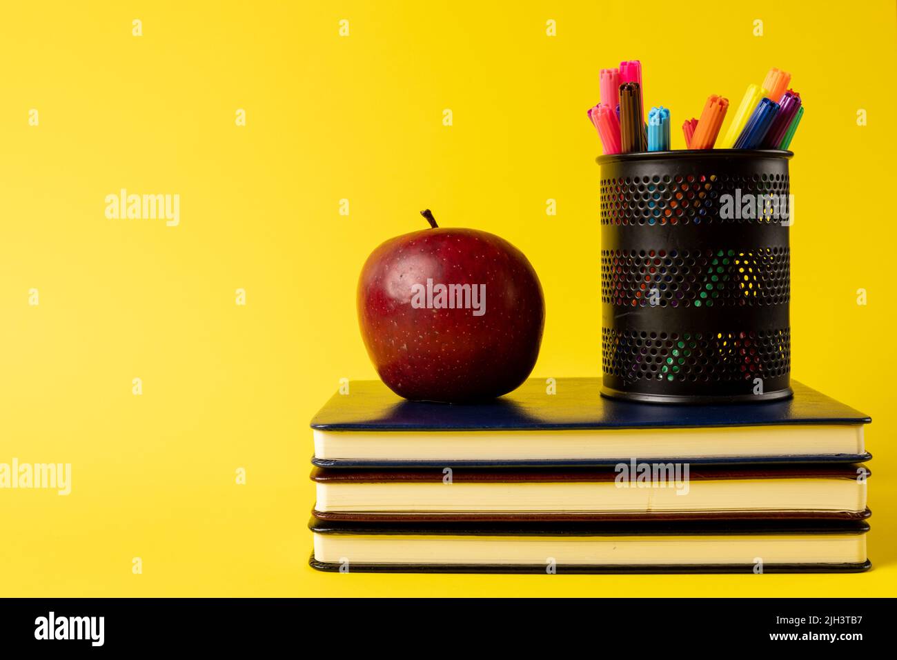 Zusammensetzung von Bücherstapel, Filzstiften im Behälter und Apfel auf gelbem Hintergrund Stockfoto