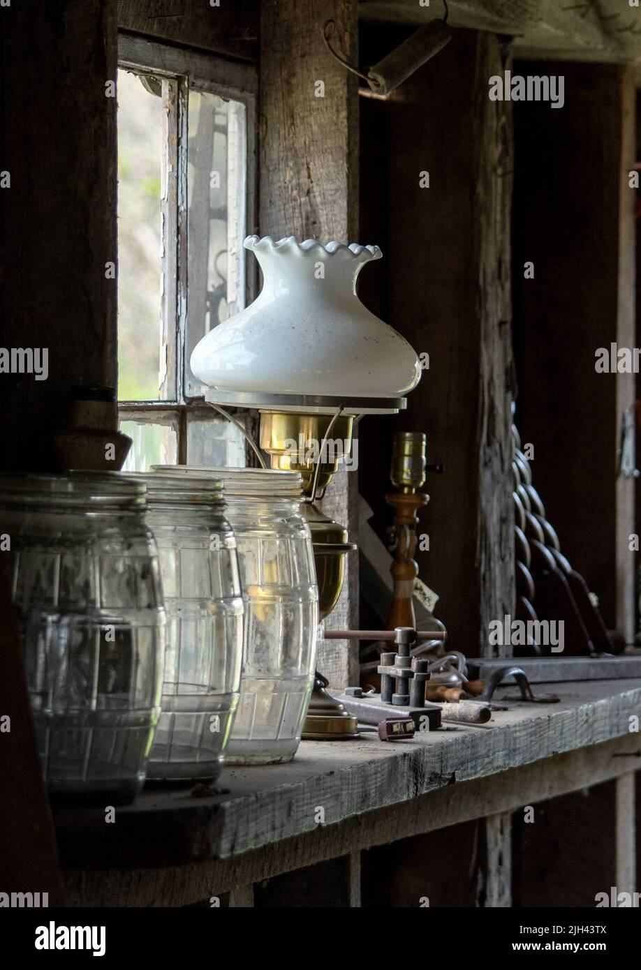 Alte Öllampen, Glasgefäße und andere Ecken und Enden werden mit natürlichem Licht aus einem alten Scheunenfenster beleuchtet Stockfoto