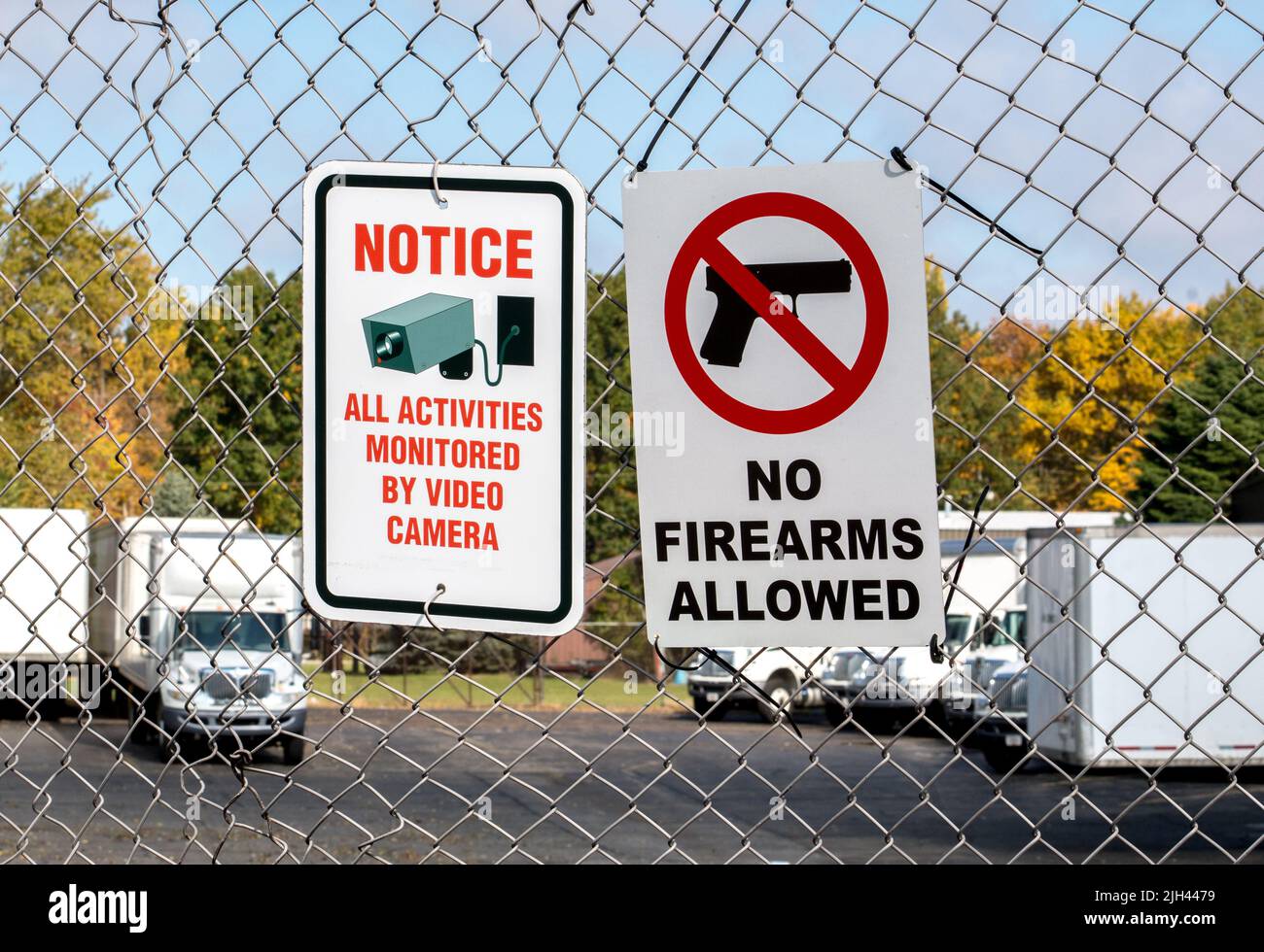 Schilder an einem Kettengliederzaun außerhalb eines Unternehmens, Feuerwaffen sind nicht erlaubt und Videokameras überwachen den Bereich. Stockfoto