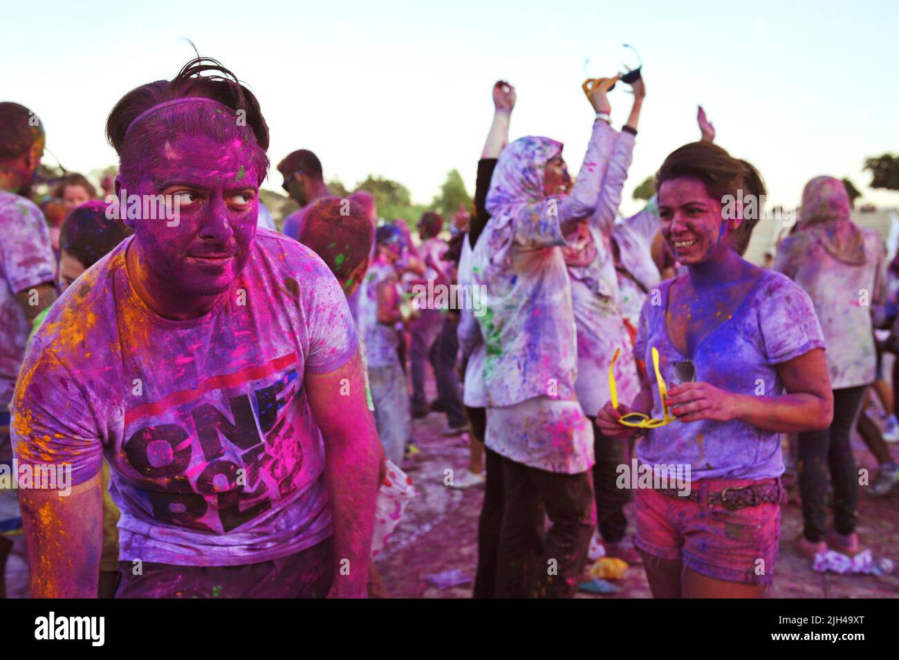 Ein junger Mann, der mit farbigem Pulver bedeckt ist, entfernt Schattierungen, um die Augen zu enthüllen, und gibt einem Freund beim Color Walk in Dubai, Vereinigte Arabische Emirate, einen lustigen Blick. Stockfoto