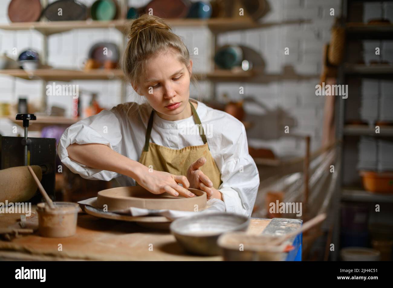 Ein Keramiker macht einen Teller. Frau in einer Schürze arbeitet in einer Töpferwerkstatt. Stockfoto