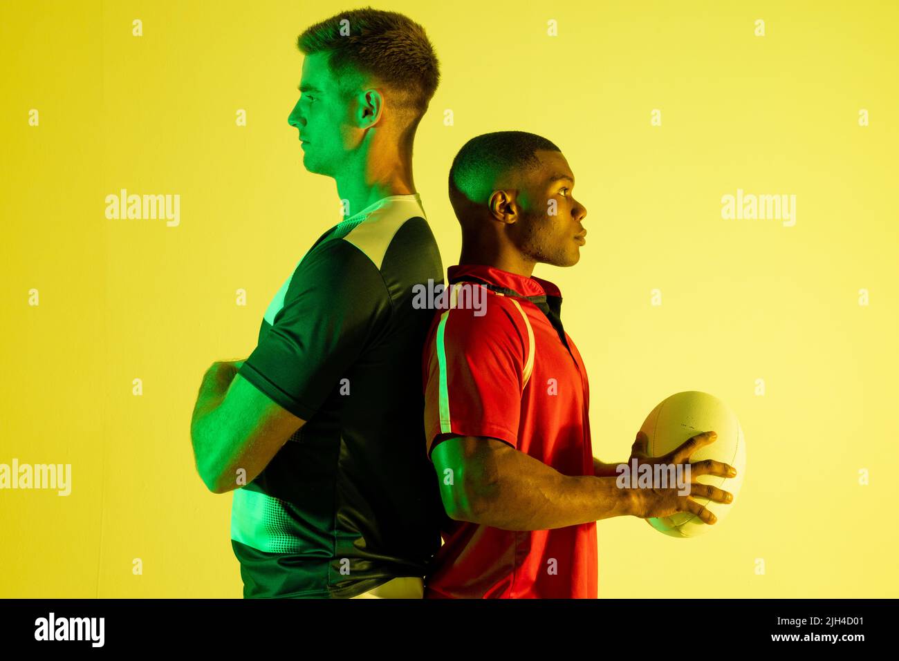 Diverse männliche Rugby-Spieler mit Rugby-Ball über gelber Beleuchtung Stockfoto
