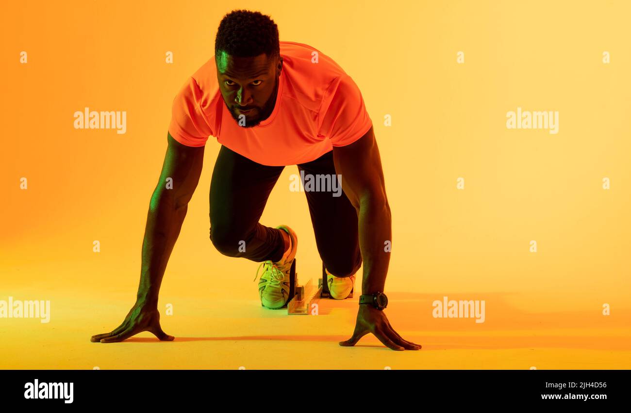 Bild eines afroamerikanischen Athleten, der sich in gelber Beleuchtung auf den Lauf vorbereitet Stockfoto