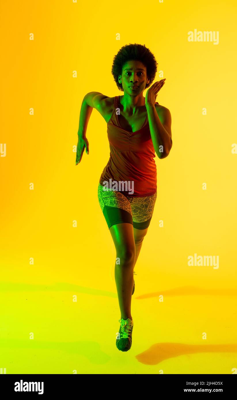 Vertikales Bild einer afroamerikanischen Sportlerin, die in gelber Beleuchtung läuft Stockfoto