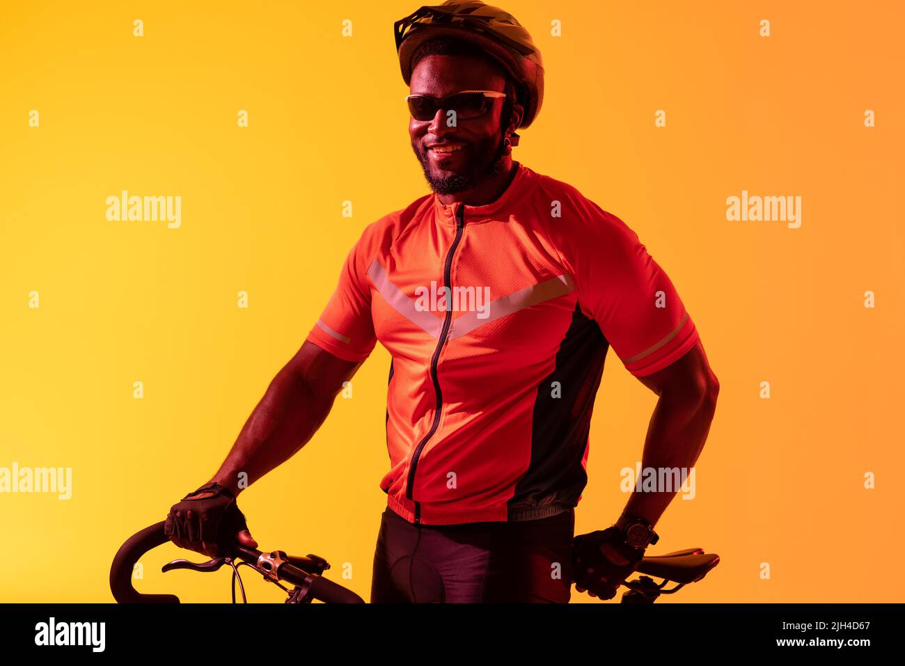 Bild eines glücklichen afroamerikanischen Radfahrers, der in gelber Beleuchtung die Kamera anschaut Stockfoto