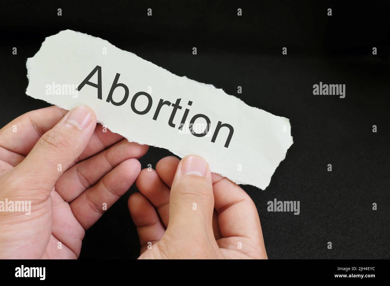 Ungewollte Schwangerschaftsabtreibung Konzept. Hand hält ein Stück Papier mit geschriebenem Wort Abtreibung auf schwarzem Hintergrund. Stockfoto