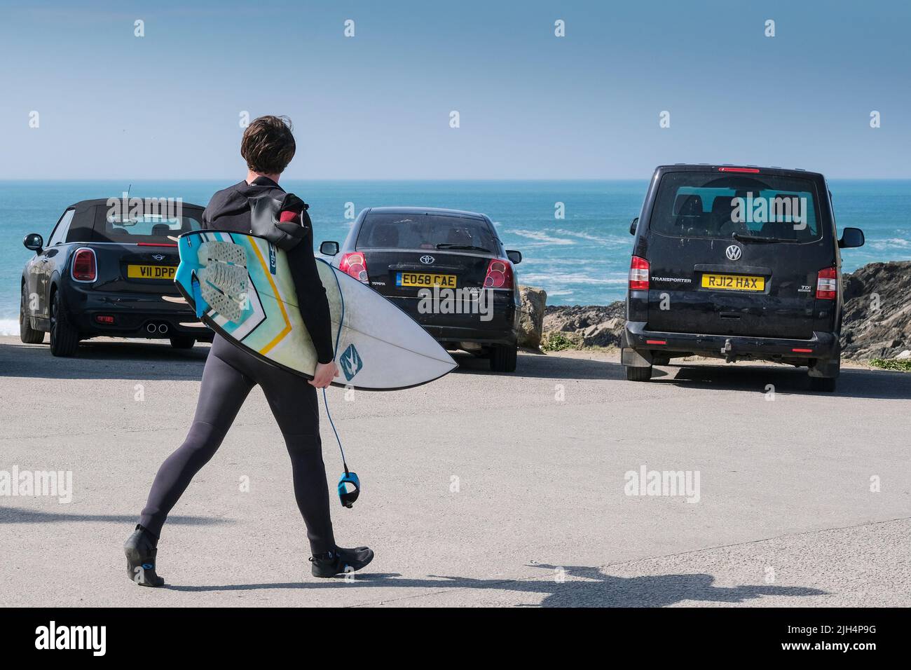 Ein Surfer, der sein Surfbrett trägt und über den Towan Head Little Fistral Parkplatz in England in Großbritannien läuft. Stockfoto